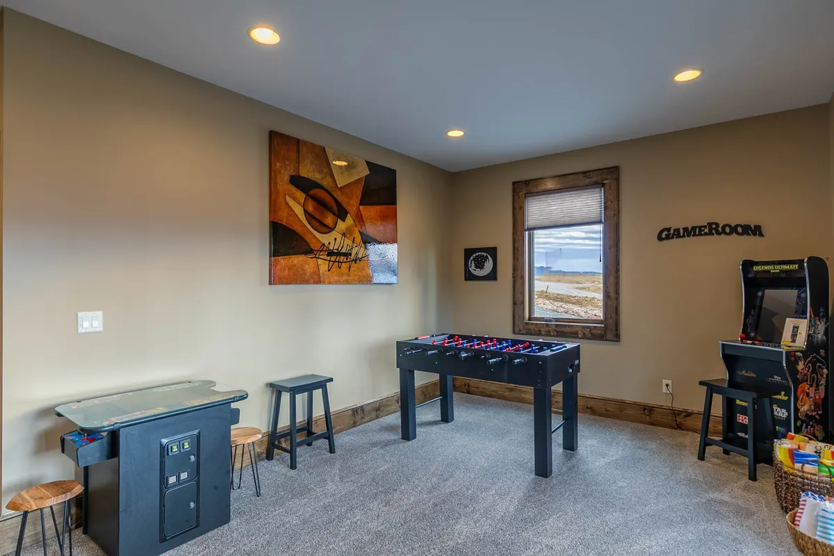 A vibrant corner of the game room featuring a foosball table, a classic arcade game machine, colorful artwork on the wall, and a couple of stools for seating. The area exudes a playful, energetic vibe ideal for gaming and social interaction.
