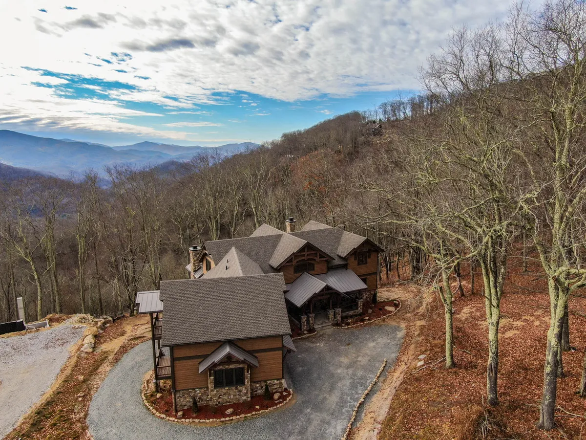 This image showcases the house nestled against a backdrop of stunning mountain views, with bare trees and a spacious driveway leading toward nature. The scene evokes tranquility and highlights the immediate access to hiking trails and natural surroundings.