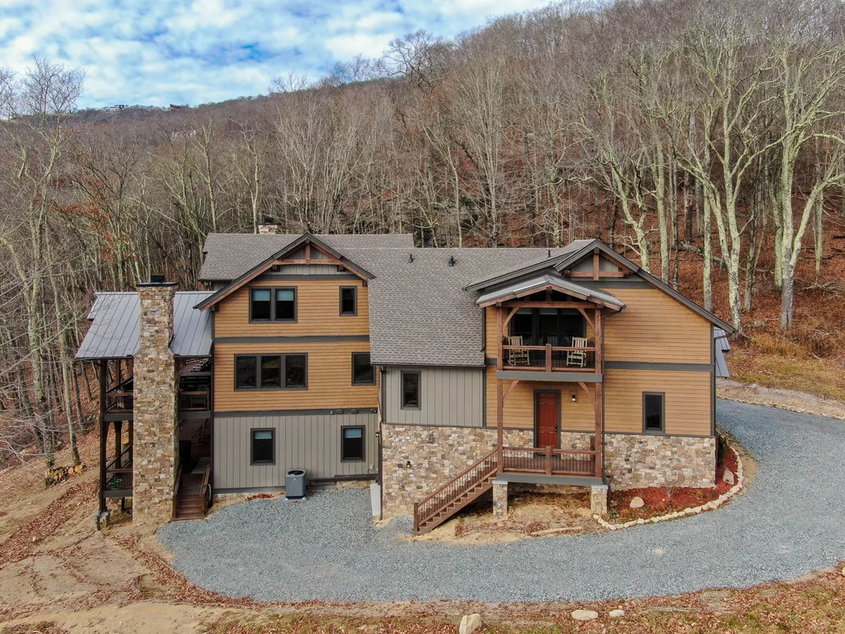 An exterior view of 5 Cubs Lodge highlights its stone facade, wooden accents, large windows, and the surrounding trees, giving a sense of seclusion and immersion in the natural landscape. The image hints at spaciousness and the outdoor amenities that might be available on the property.