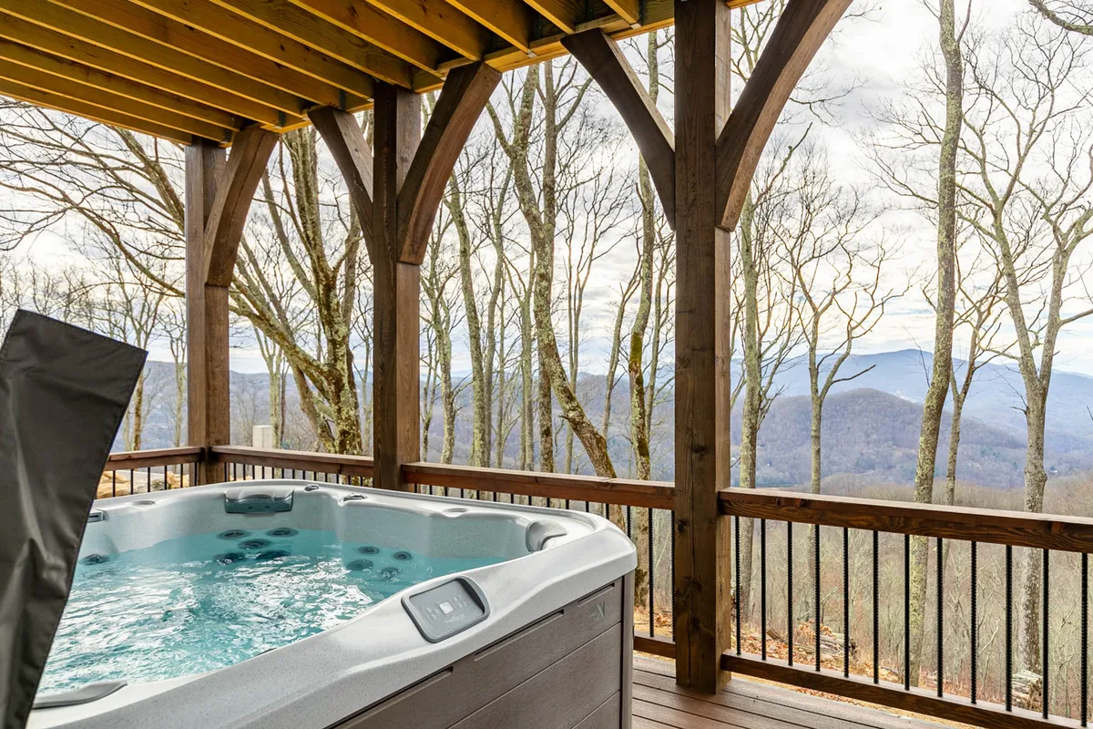 An inviting exterior shot featuring a private hot tub set against a backdrop of mountain views and surrounding trees. The wooden structure adds rustic charm, emphasizing relaxation and natural beauty.