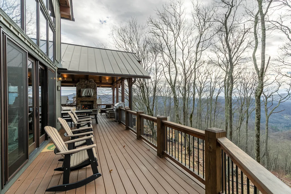 A serene deck scene featuring wooden chairs arranged around an outdoor fireplace. The deck overlooks sweeping mountain landscapes, inviting guests to relax and soak in the views at sunset or during cozy evenings by the fire.