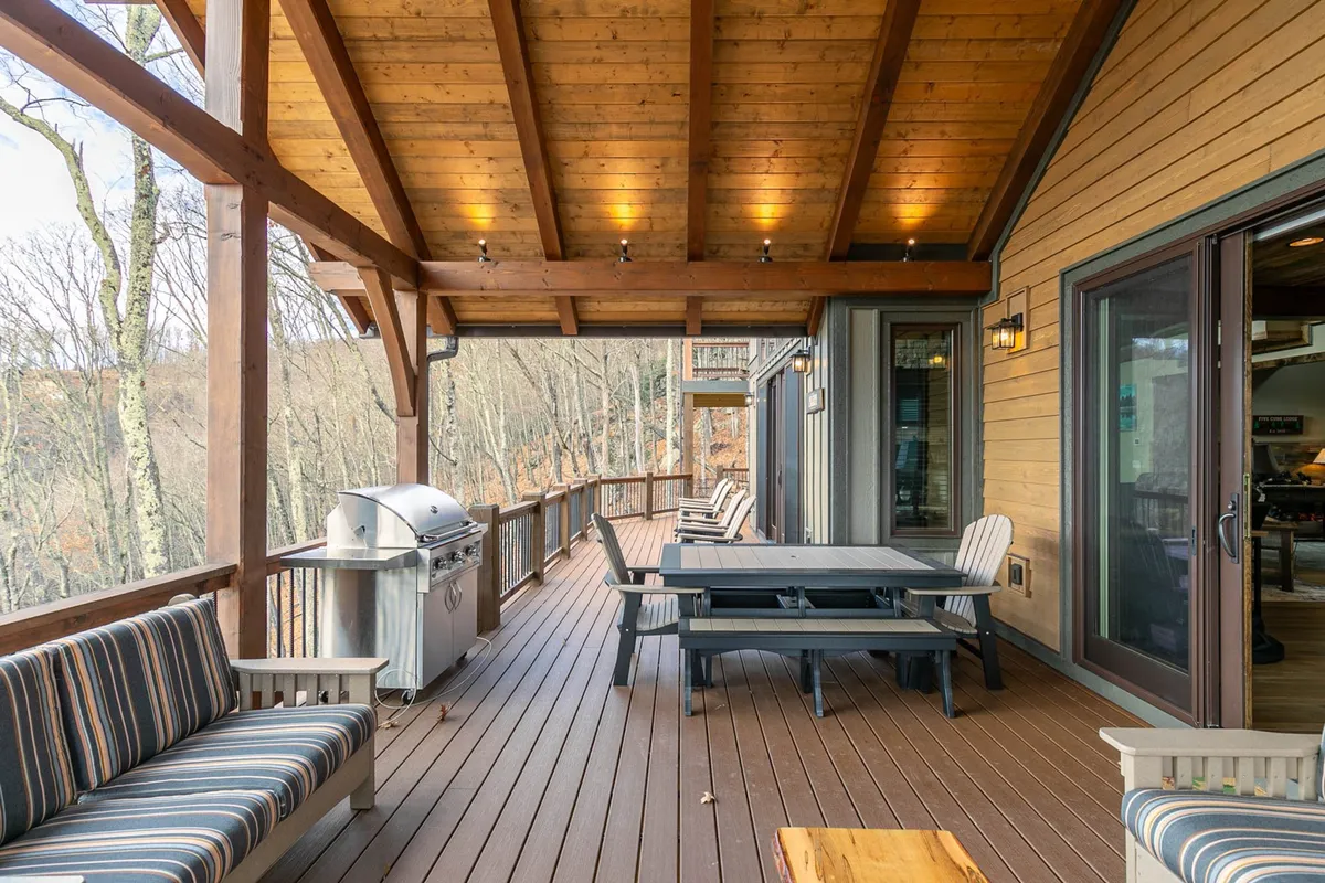 A welcoming covered outdoor dining area features wooden beams, a grill, striped cushions, and a spacious table, inviting groups to gather for meals, barbecues, and social events in the fresh air.