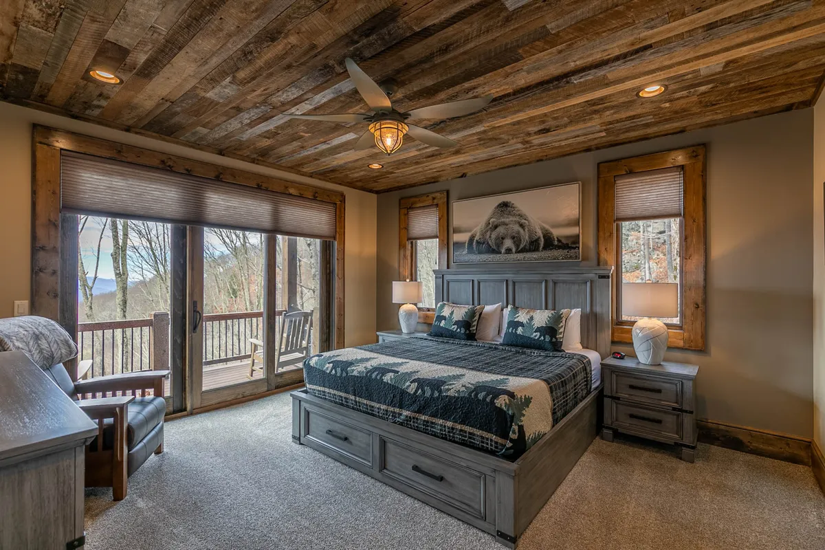 A spacious bedroom featuring a large bed with a patterned blanket, rustic wooden ceiling, and expansive windows that invite mountain views. The room is styled with cozy, inviting furniture, optimizing both comfort and visual appeal.