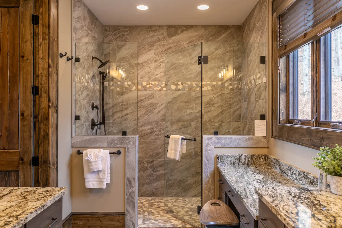 A modern ensuite bathroom featuring a large glass shower enclosure, granite countertops, wooden accents, and stone tiles, creating a luxurious yet calming atmosphere perfect for relaxing after a day outdoors.