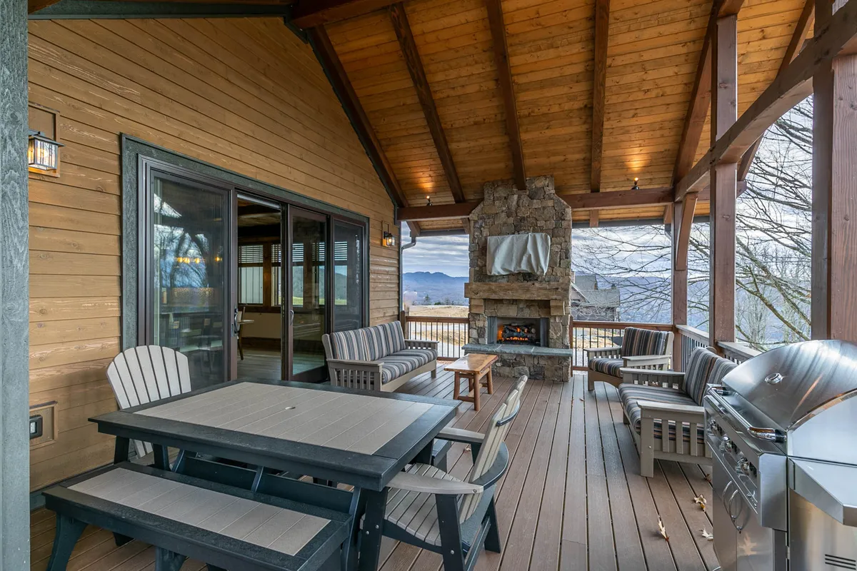 A welcoming outdoor living area features a large stone fireplace, grill, and a spacious dining table. Comfortable seating invites guests to gather for barbecues, enjoy sunset views, or share stories around the fire, all set against a backdrop of natural mountain beauty.