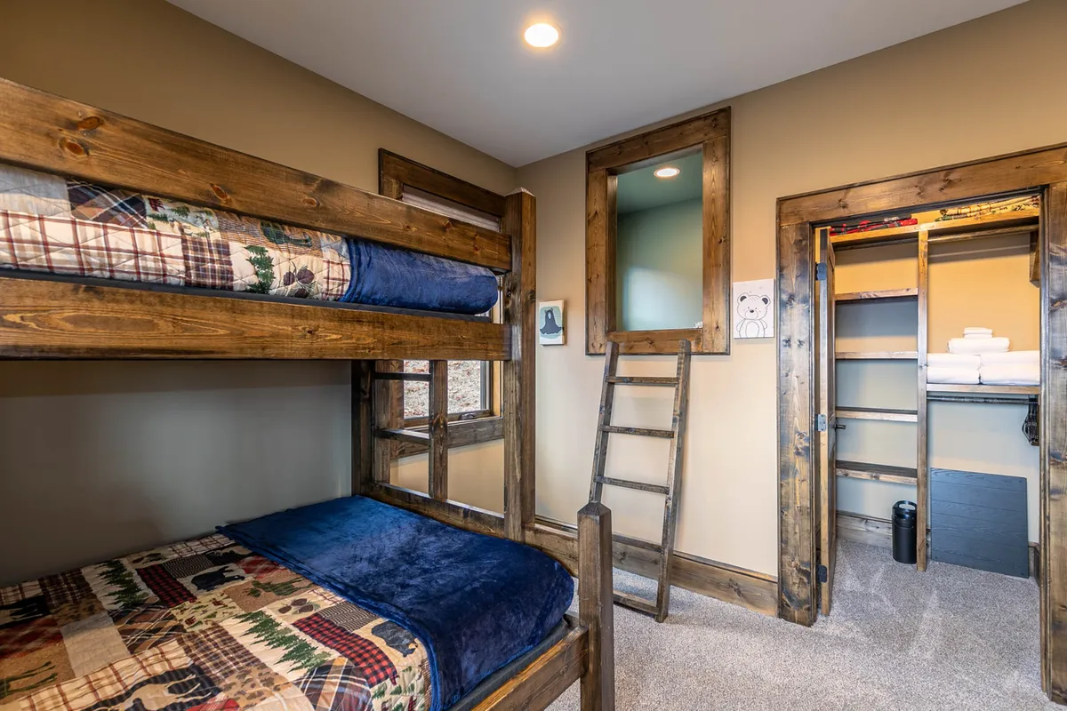 A playful bunk room equipped with twin-over-full bunk beds, a sturdy ladder, and a closet—set in a welcoming, cozy environment ideal for children and teens. The space exudes a sense of fun and togetherness.